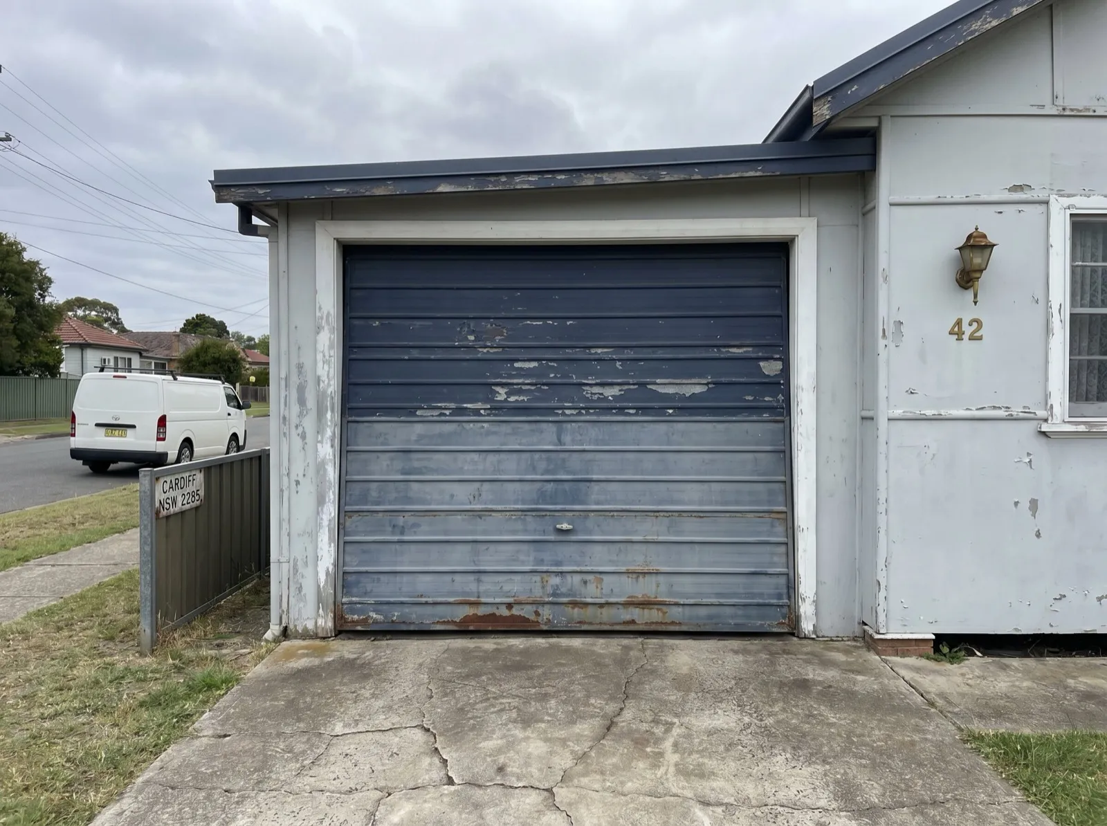 An aged original garage door with faded paint and rust along the bottom edge on a post-war fibro house