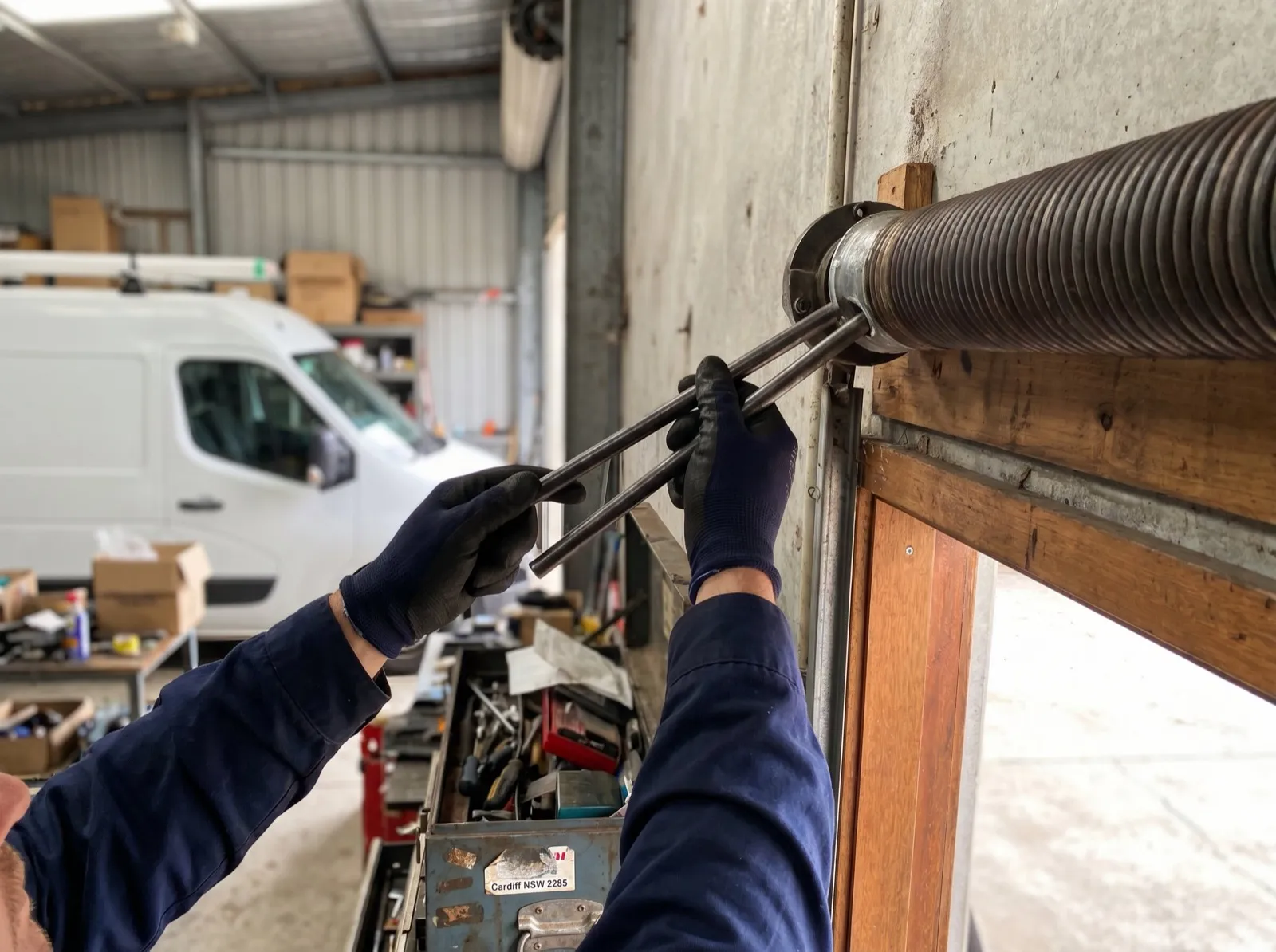 Gloved hands fitting steel winding bars to the winding cone of a torsion spring